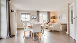 A spacious living room with a dining area, featuring a large window, a flat-screen TV, and a cozy seating arrangement. - Watthüs Wenningstedt - Wenningstedter Superlativ (Wenningstedt-Braderup (Sylt))