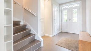 A staircase with dark tiles, white walls, and a beige carpet leading to a door with a decorative glass panel. - Watthüs Wenningstedt - Wenningstedter Superlativ (Wenningstedt-Braderup (Sylt))