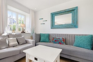 A modern living room with a grey sofa, white coffee table, and teal cushions.