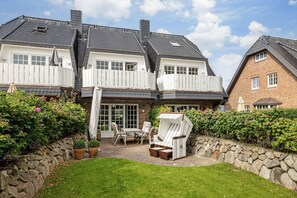 Ett tvåvåningshus med en balkong, en uteplats med utemöbler och en stenmur som omger trädgården.