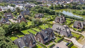 An aerial view of a residential area with houses, green lawns, and a body of water. - Landhaus Weidenstieg, App. 2 - Luxus und Wohlfühlen am Dorfteich (Wenningstedt-Braderup (Sylt))