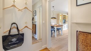 A hallway with wooden hangers and a black bag, leading to a dining area with a table and chairs. - Landhaus Weidenstieg, App. 2 - Luxus und Wohlfühlen am Dorfteich (Wenningstedt-Braderup (Sylt))