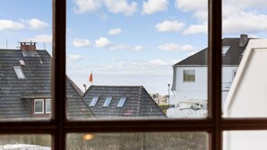 A view through a window of a residential area with multiple houses, a flag, and a clear sky. - Atlantik, App. 10a - Helles Appartement im 1. Obergeschoss, ca. 29 qm Nutzfläche für 2 Personen (Wenningstedt-Braderup (Sylt))