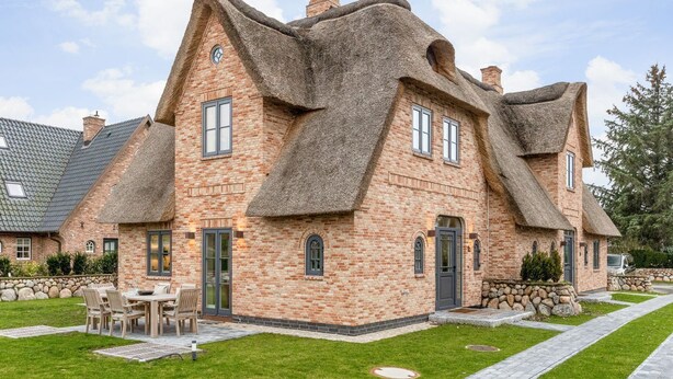 Ein Haus aus Backsteinen mit strohgedecktem Dach und einem steinernen Fundament.