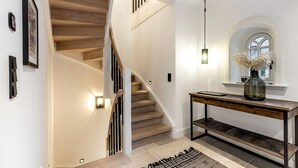 Eine moderne Treppe mit Holzboden und schwarzen Geländern, ein Konsolentisch mit einer Vase sowie eine Wandleuchte.