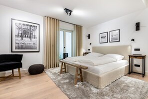 Quarto moderno com uma cama grande, escrivaninha e cadeira. Há quadros nas paredes e uma janela com cortinas.