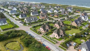 Eine Vogelperspektive auf ein Küstendorf mit traditionellen Häusern, einer Straße und einem Hotel.