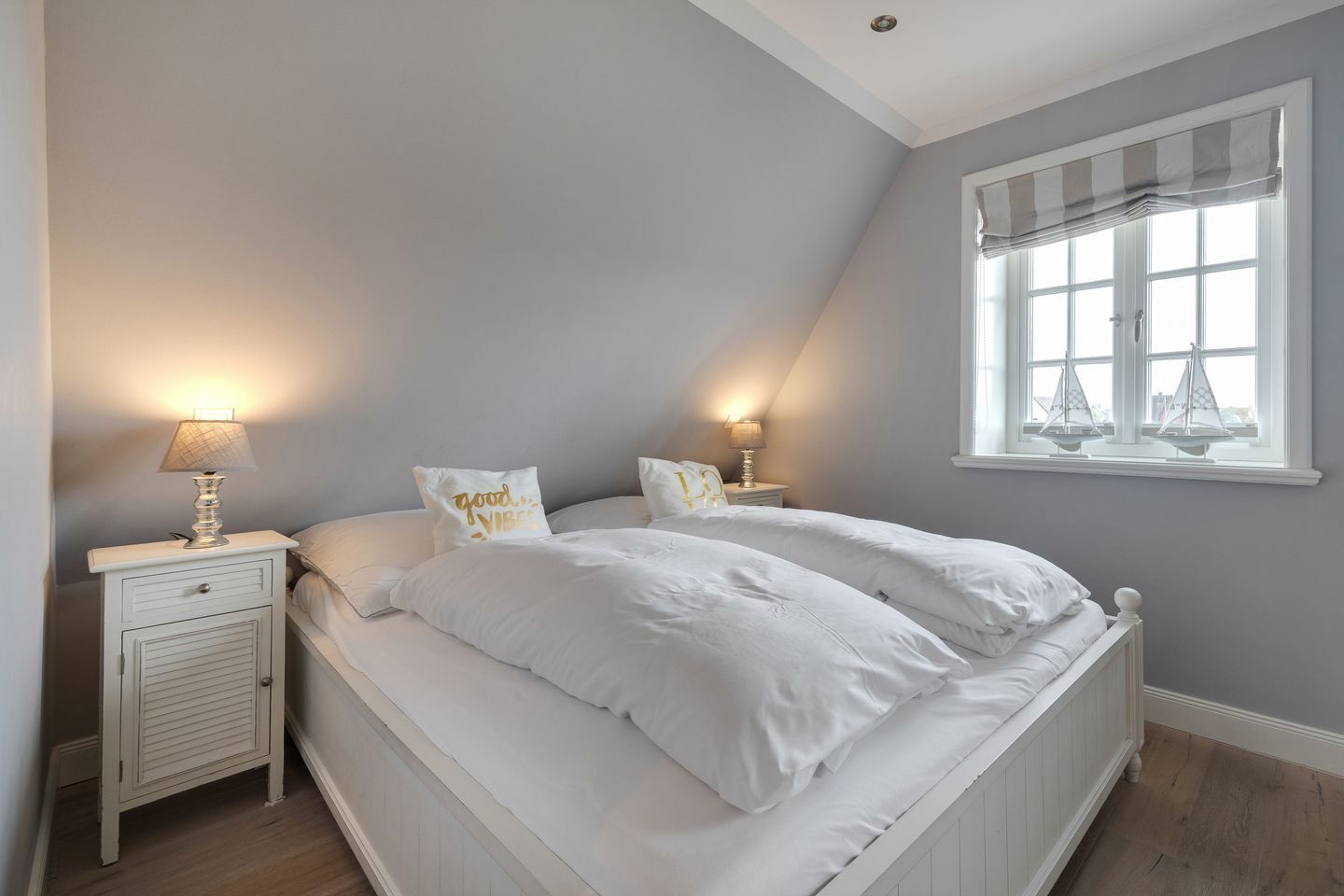 A bedroom with a bed, two nightstands, a window with curtains, and a lamp on each nightstand.
