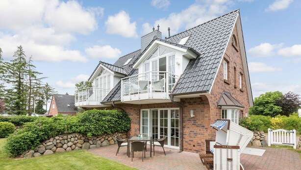 Une maison à deux étages avec un balcon, une terrasse dotée de mobilier d’extérieur et un mur en pierre.