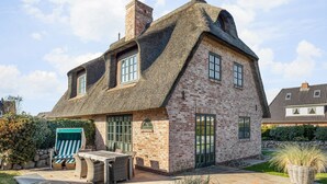A two-story house with a thatched roof, brick walls, and a patio with outdoor furniture. - Sylt-hues - Lifestyle Unter Reet, Strand & Meer um die Ecke. Ihr Optimales Urlaubs-domizil (Wenningstedt-Braderup (Sylt))