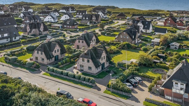 A coastal residential area with houses featuring thatched roofs and stone walls, surrounded by well-maintained gardens and a clear view of the sea. - Sylt-hues - Lifestyle Unter Reet, Strand & Meer um die Ecke. Ihr Optimales Urlaubs-domizil (Wenningstedt-Braderup (Sylt))