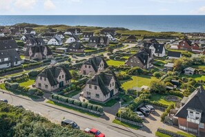 Ein Küstenwohngebiet mit Häusern, deren Dächer mit Stroh gedeckt und deren Wände aus Stein sind, umgeben von gepflegten Gärten und freiem Blick auf das Meer.