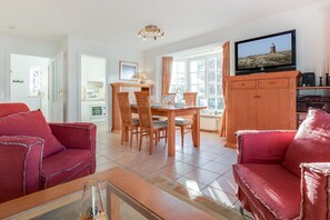 A spacious living area with a dining table, two red sofas, a television, and a kitchen in the background. - Christopher, App. 5 - Charmanter Luxus mit Flair (Wenningstedt-Braderup (Sylt))