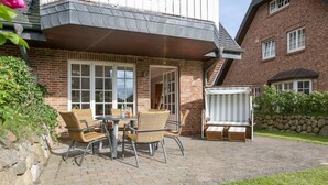 Une terrasse avec des chaises et une table en osier, un espace salon couvert et un mur en pierre.