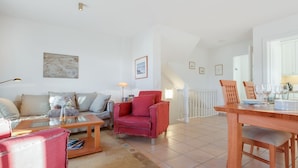 Un salon spacieux comprenant un canapé, un fauteuil rouge, une table à manger en bois et un escalier menant à un autre niveau.