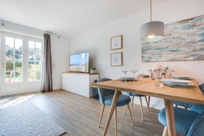 A dining area with a wooden table set for six, a television on a white cabinet, and a large abstract painting on the wall.
