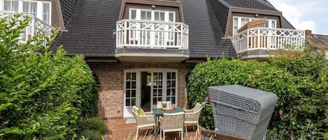 Une maison à deux étages dotée d’un balcon, d’une terrasse avec mobilier d’extérieur et d’un jardin bien entretenu.