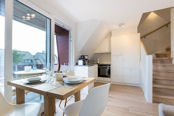 A modern kitchen with white cabinets, a wooden dining table, and a staircase leading to an upper level.
