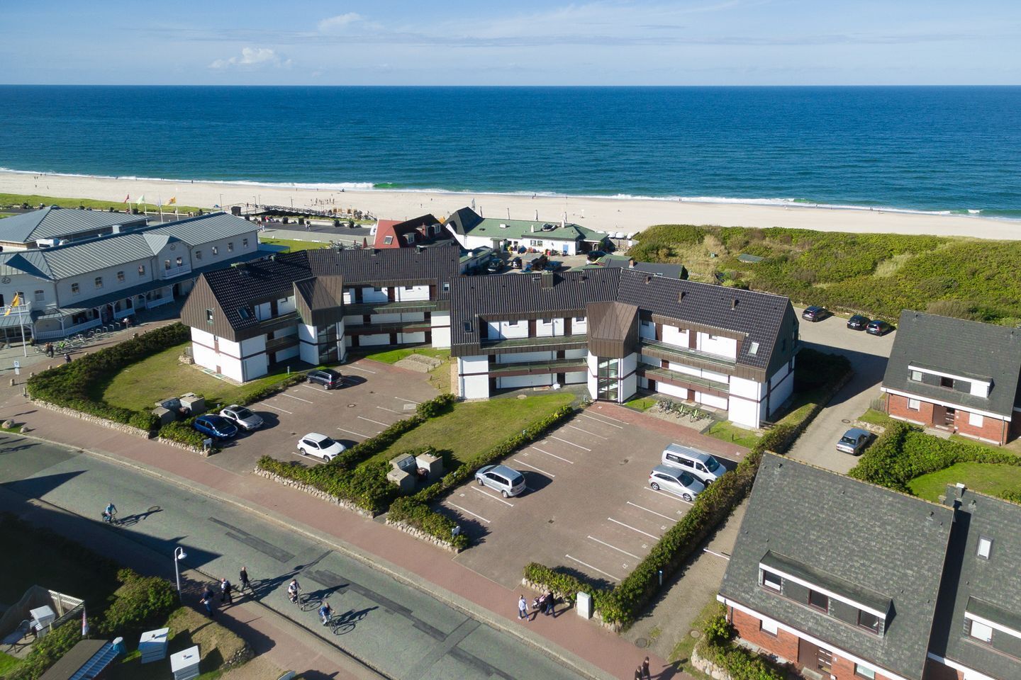 Ein Luftbild eines Küstenhotels mit mehreren Gebäuden, Parkplätzen und einem Strand im Hintergrund.