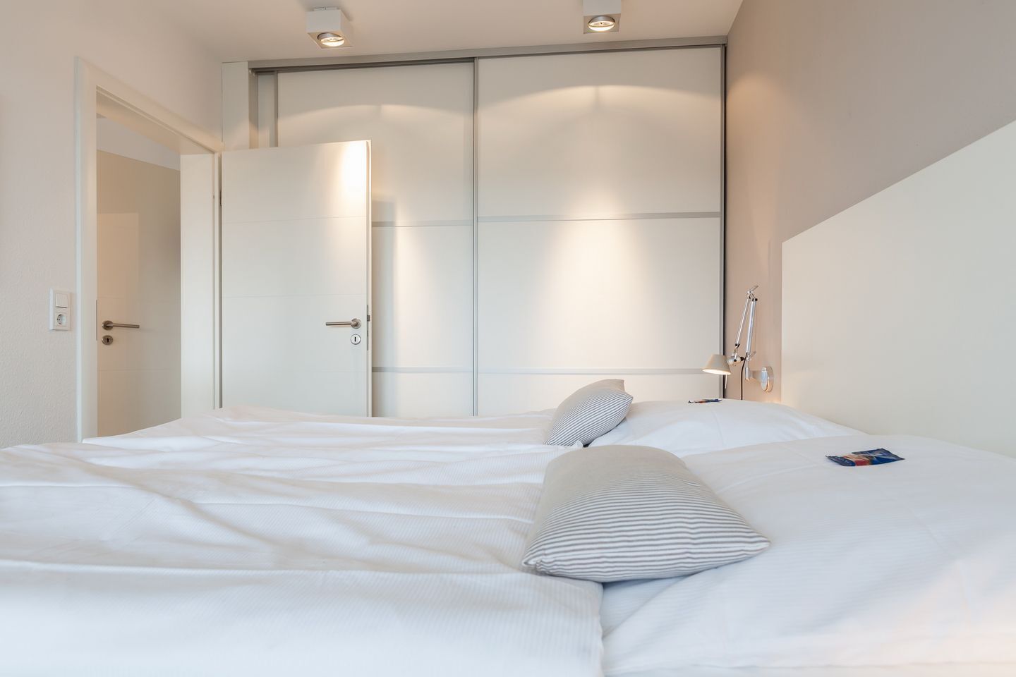 A hotel room with a large bed, a wardrobe, and a bedside table with a lamp.