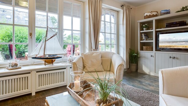 A cozy living room with a large window, a sailboat model, a television, and a comfortable sofa. - Christopher, App. 6 Strönhüs - Urlaubsfeeling Pur. Mit Äußerst Viel Liebe zum Detail (Wenningstedt-Braderup (Sylt))