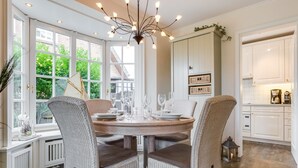 A dining area with wicker chairs, a round wooden table set for six, and a modern chandelier. - Christopher, App. 6 Strönhüs - Urlaubsfeeling Pur. Mit Äußerst Viel Liebe zum Detail (Wenningstedt-Braderup (Sylt))