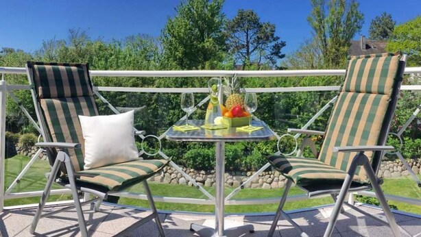 Two striped lounge chairs with cushions, a small round table with a fruit bowl and wine glasses, and a clear view of a well-maintained garden and trees in the background. - Landhaus Normannenweg, App. 4D - In Zentraler und Ruhiger Lage Gelegenes 3-raum Appartement im OG- (Wenningstedt-Braderup (Sylt))