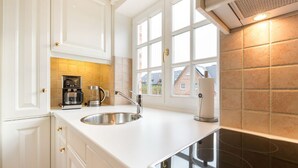 A modern kitchen with white cabinetry, a stainless steel sink, a coffee maker, and a built-in stove. - Landhaus Normannenweg, App. 4D - In Zentraler und Ruhiger Lage Gelegenes 3-raum Appartement im OG- (Wenningstedt-Braderup (Sylt))