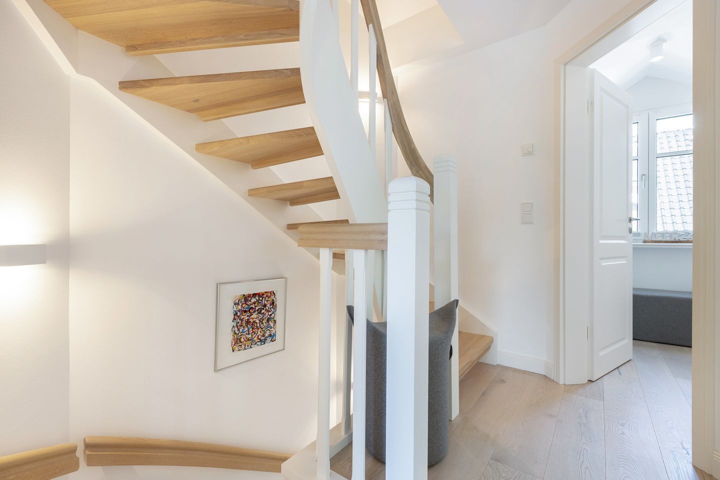 Una escalera moderna con escalones de madera y barandillas blancas, que conduce a una habitación con un banco y una ventana.