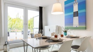 A dining area with a table set for two, a potted plant, and a painting of a lighthouse. - Badezeit - Verbringen Sie Ruhige Tage in Modernem, Designorientiertem Ambiente (Wenningstedt-Braderup (Sylt))