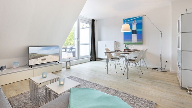 A modern living room with a TV, dining area, and a painting of a lighthouse. - Badezeit - Verbringen Sie Ruhige Tage in Modernem, Designorientiertem Ambiente (Wenningstedt-Braderup (Sylt))