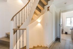 A modern staircase with wooden steps and white walls, leading to a well-lit room.