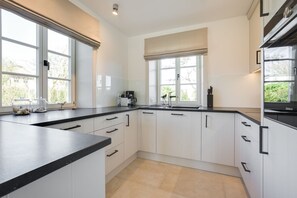 A modern kitchen with white cabinets, black countertops, and large windows. - Marysol - Erleben Sie Ihren Urlaub im Typischen Sylt-stil Unter Reet (Wenningstedt-Braderup (Sylt))