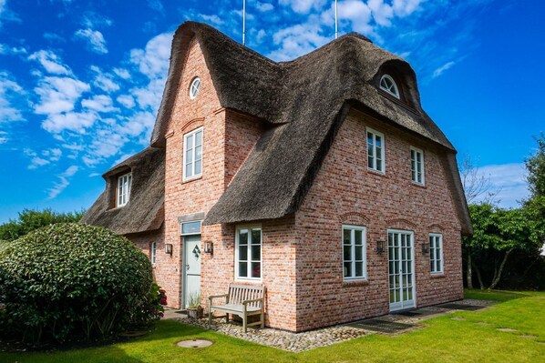 A brick house with a thatched roof, a front door, and a bench outside.