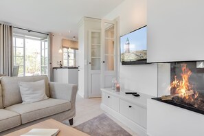 Ein modernes Wohnzimmer mit Kamin, einer Couch, einem an der Wand befestigten Fernseher und einer Küche im Hintergrund.