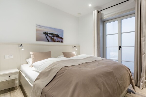 A bedroom with a large bed, bedside tables, a nightstand, a window with curtains, and a painting on the wall.