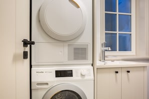 A compact, modern laundry room with a front-loading washing machine, a dryer, and a window with a view of the outside.