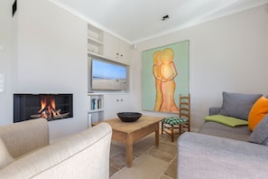A living room with a fireplace, a painting, a television, and a dining area.