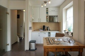 Et lille køkken med hvide skabe, kaffemaskine og et spisebord med et mønstret borddække.