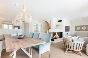 A modern living room with a wooden dining table, blue chairs, a fireplace, and a hanging light fixture.