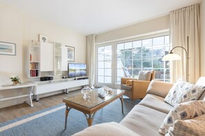 Uma sala de estar moderna com um sofá, uma mesa de centro de vidro, uma televisão e uma estante de livros.