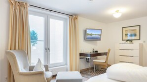 Et hotelværelse med en seng, et skrivebord med stol, et fjernsyn og et skab.