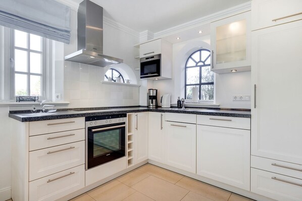 A modern kitchen with white cabinetry, a built-in oven, a microwave, and a large window with a view.