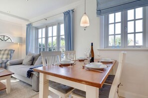 Uma sala de jantar com uma mesa de madeira posta para quatro pessoas, um sofá e um abajur.