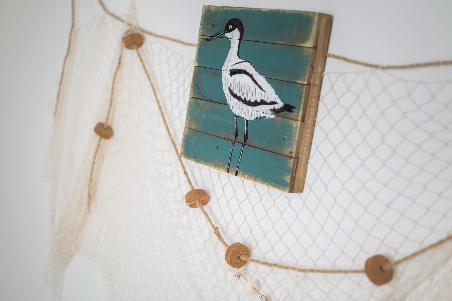 Een muur met een net en een houten paneel waarop een vogel afgebeeld is.