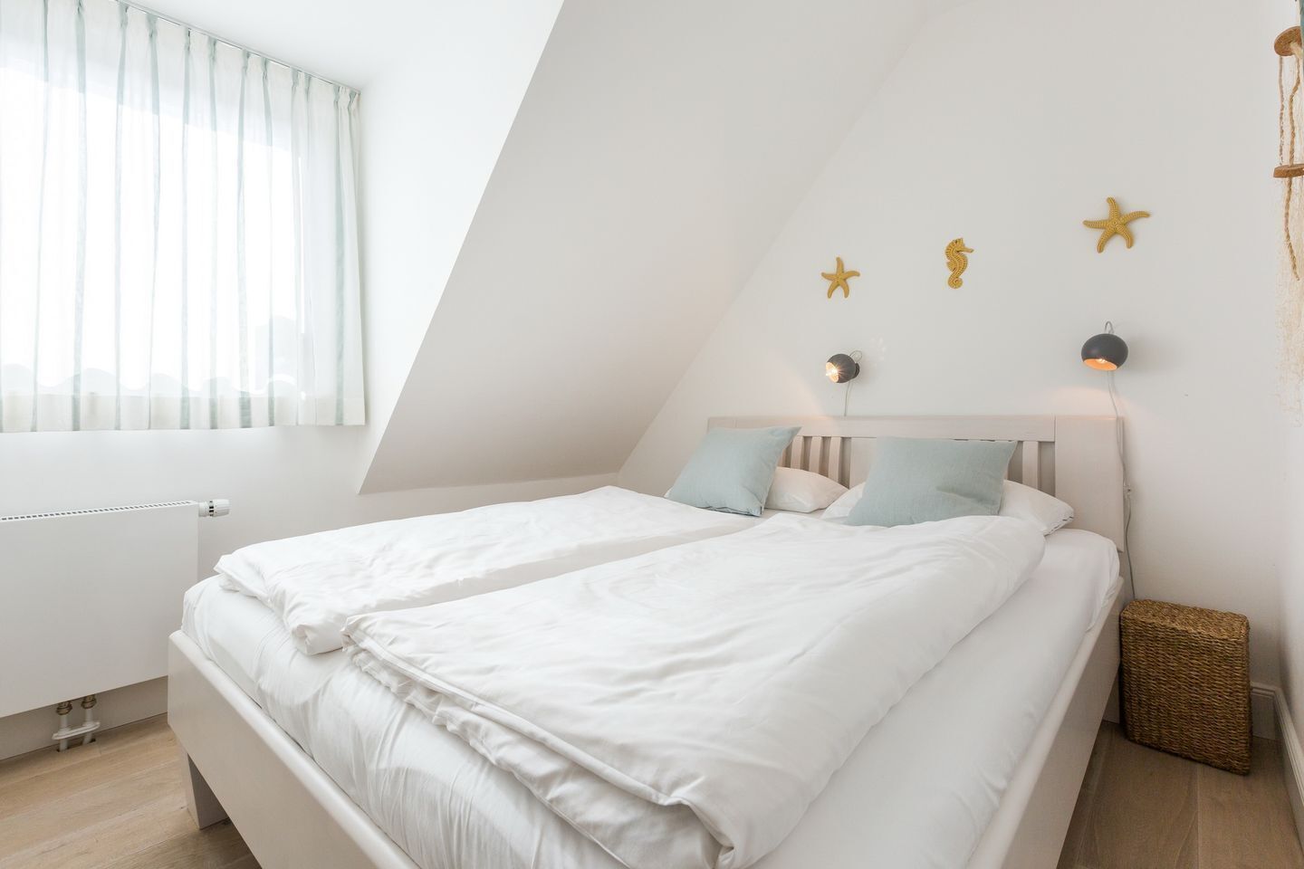 Une chambre avec un plafond en pente, un lit avec une literie blanche, une lampe de chevet et des étoiles de mer décoratives accrochées au mur.