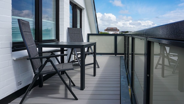 A balcony with a table and chairs, a white building, and a clear sky. - Wallhof, App. 6 - Urlauben und Relaxen im Haus Wallhof - Genießen Sie Sylt in Vollen Zügen (Wenningstedt-Braderup (Sylt))