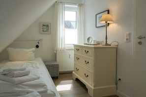 A bedroom with a bed, a dresser, a radiator, a window with curtains, and a lamp.