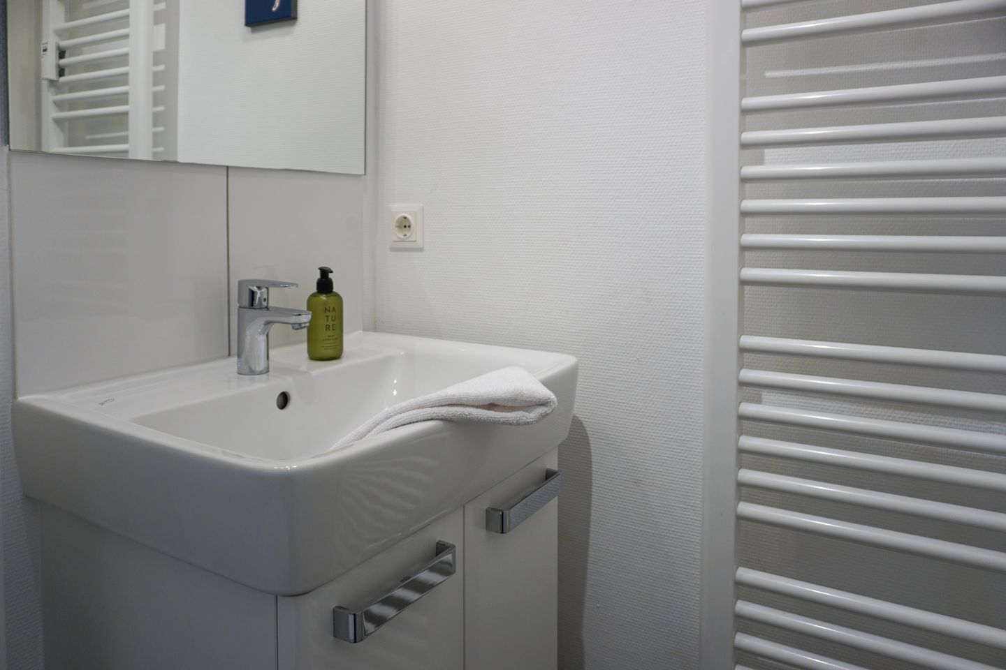 A bathroom with a white sink, a mirror, a towel, and a bottle of lotion.
