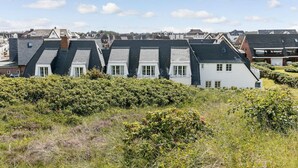A row of houses with steeply pitched roofs, surrounded by dense shrubbery.
